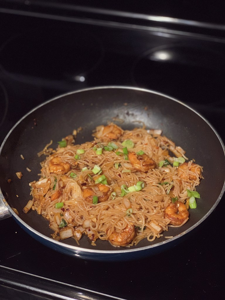 a stove-top pan filled with sauteed spicy shrimp and vermicelli noodles, topped with chopped green onion