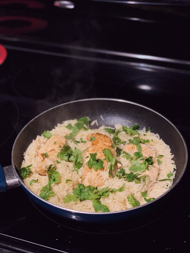 a stove-top pan filled with yellow sauteed basmati rice with chicken, topped with cilantro