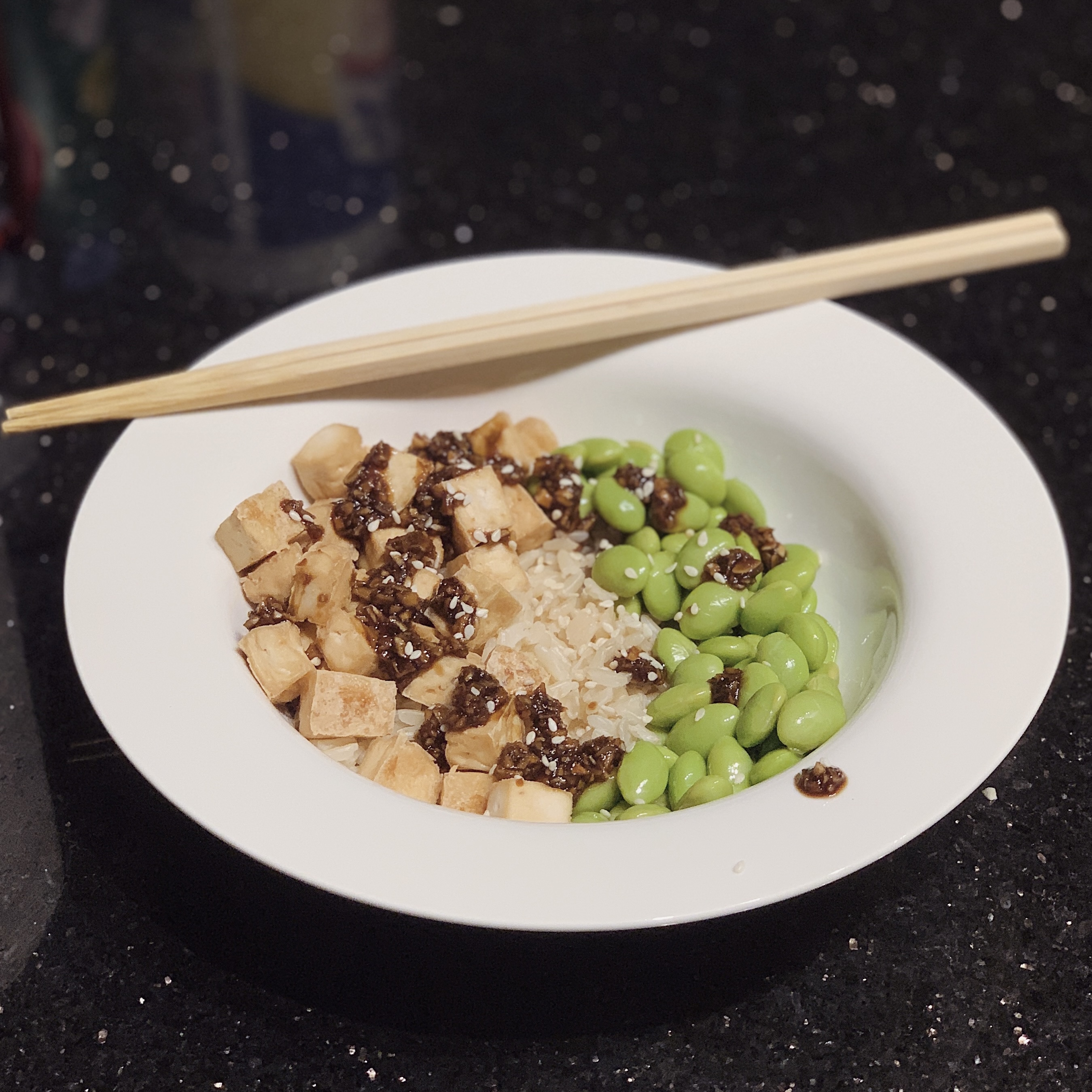 a photo of a bowl of Garlicky Baked Tofu with brown rice, edamame and a soy sauce drizzle