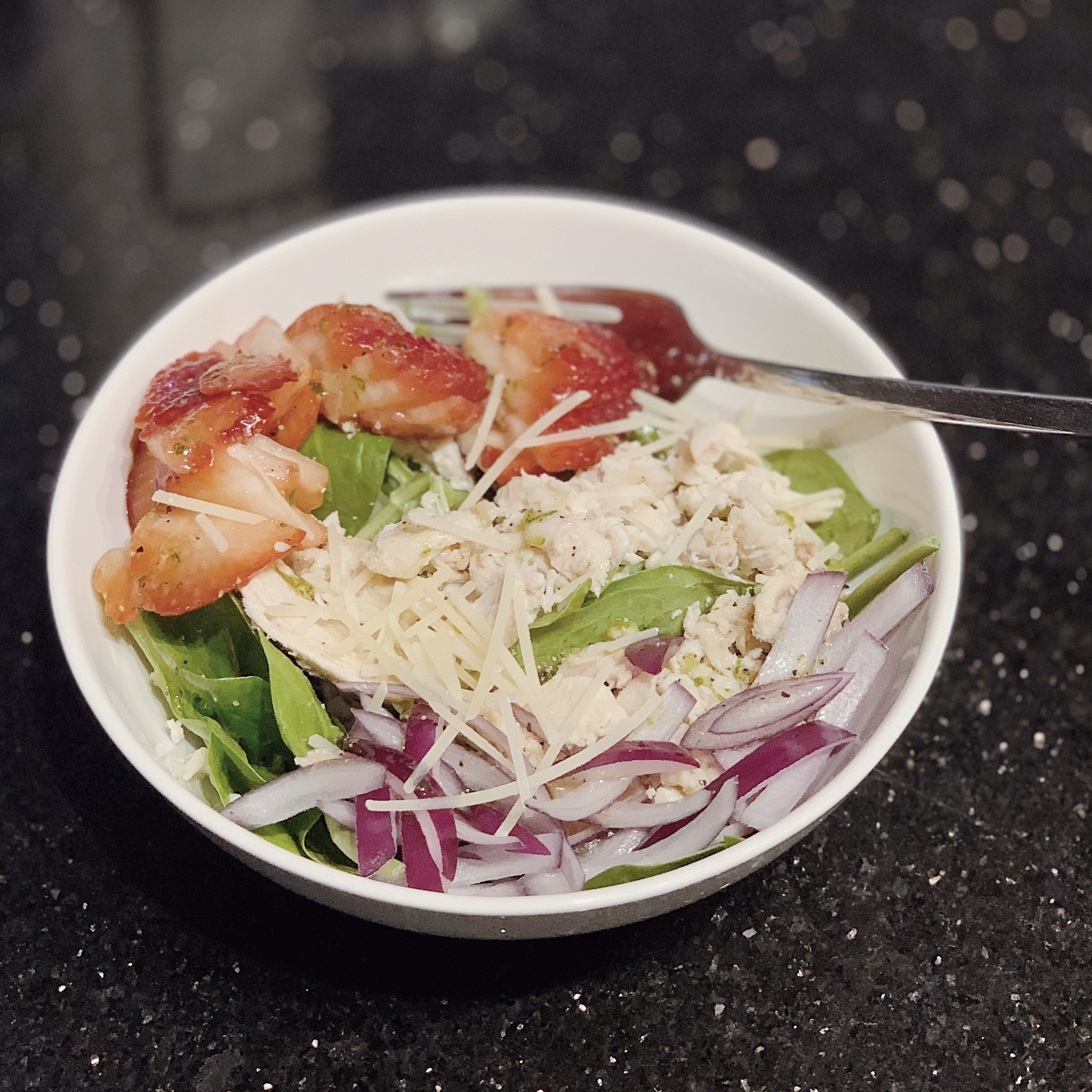 a photo of a Strawberry Cobb Salad with mixed greens, chicken, sliced strawberries, chopped red onions and sprinkled parmesan cheese