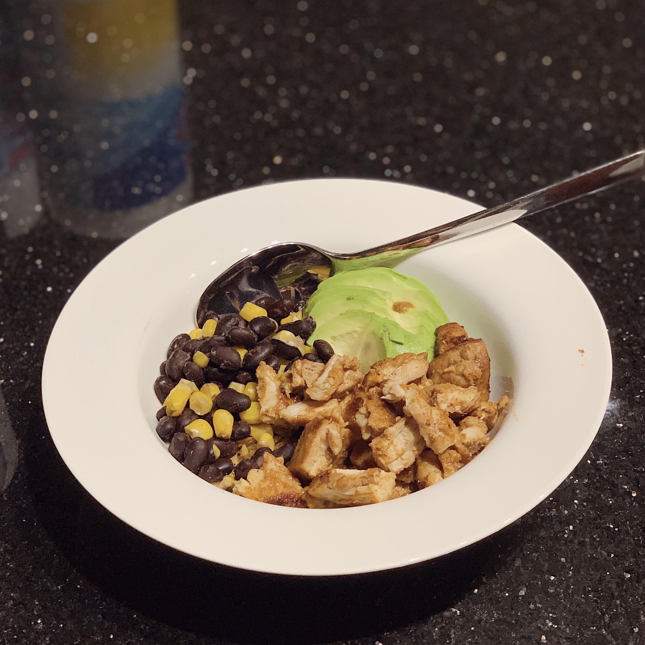 a bowl of a chicken bowl with sliced avocado, beans and corn