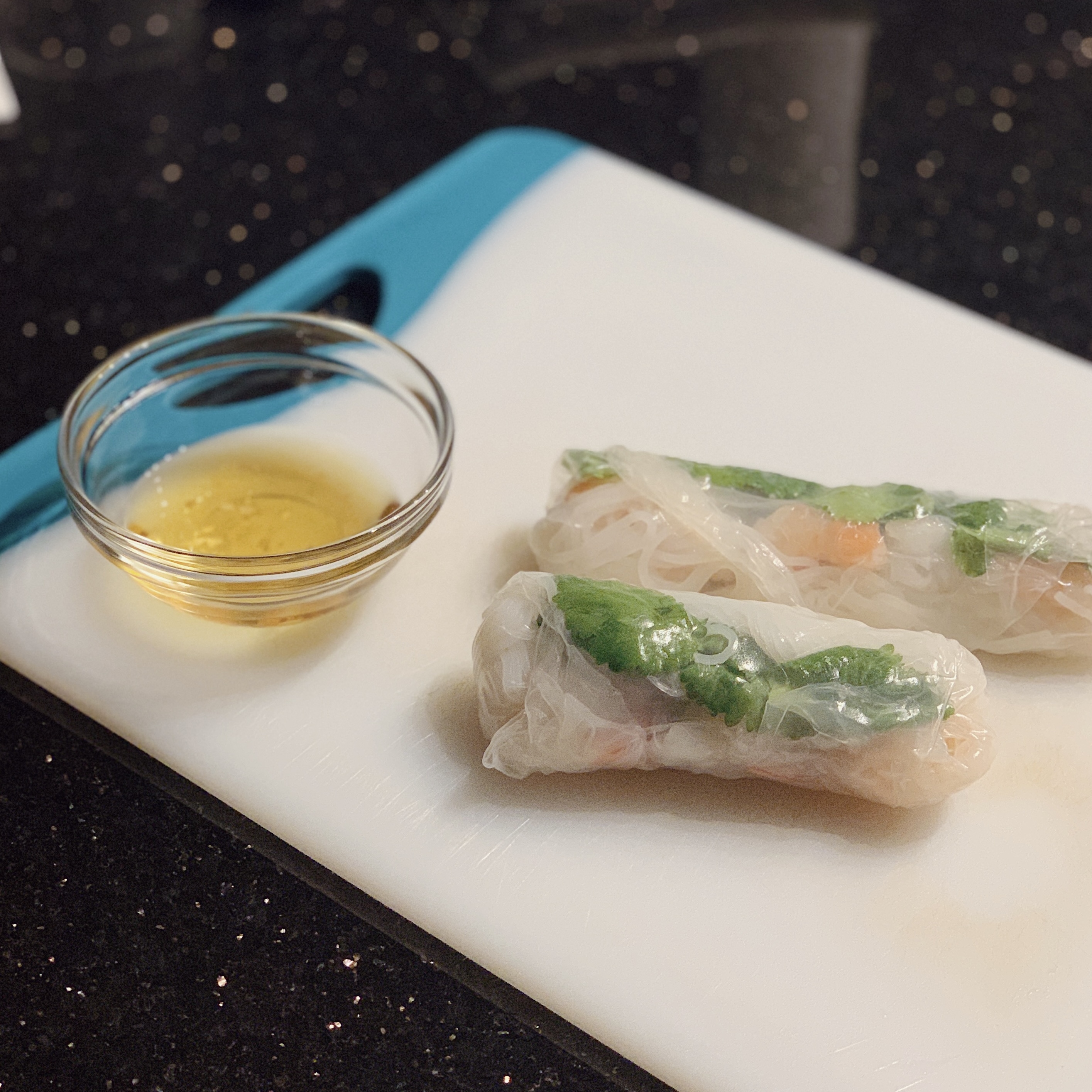 a cutting board with two shrimp spring rolls and fish dipping sauce