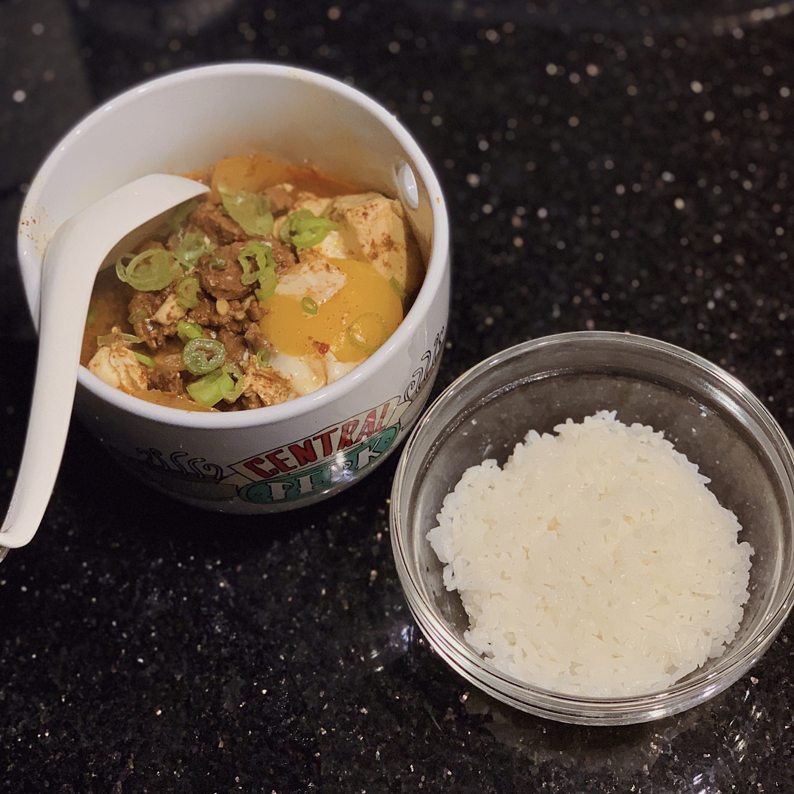 A bowl of kimchi soondubu jigae and a bowl of white jasmine rice.