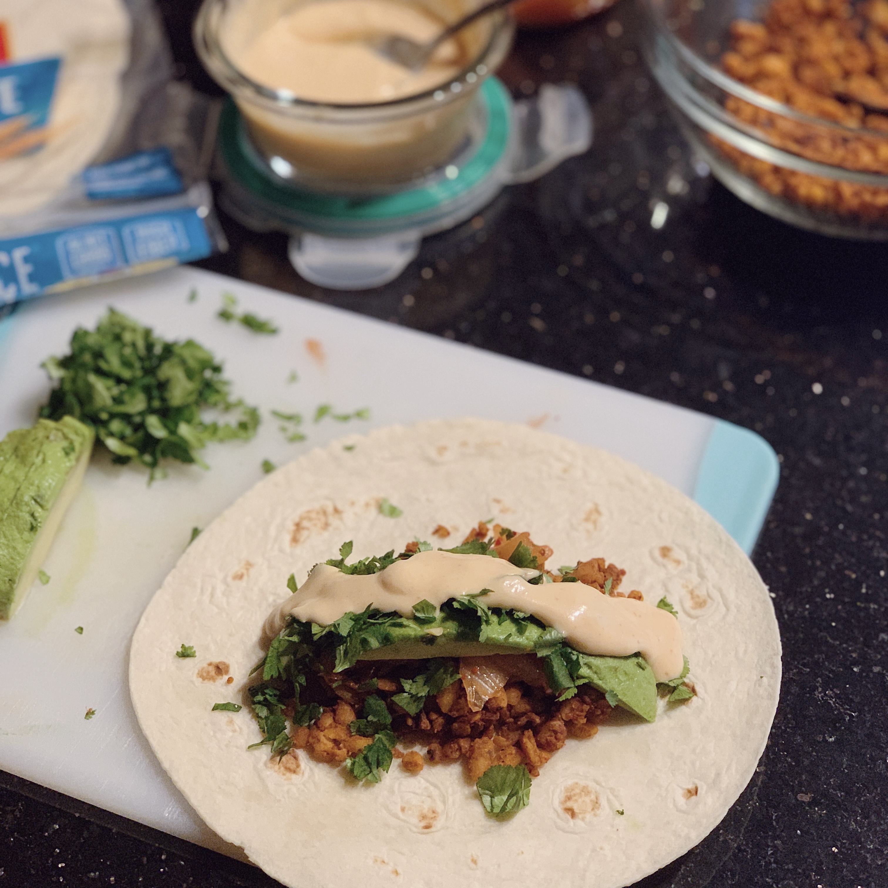 A tortilla with kimchi, tempeh, avocado, cilantro and sauce for a kimchi tempeh taco.