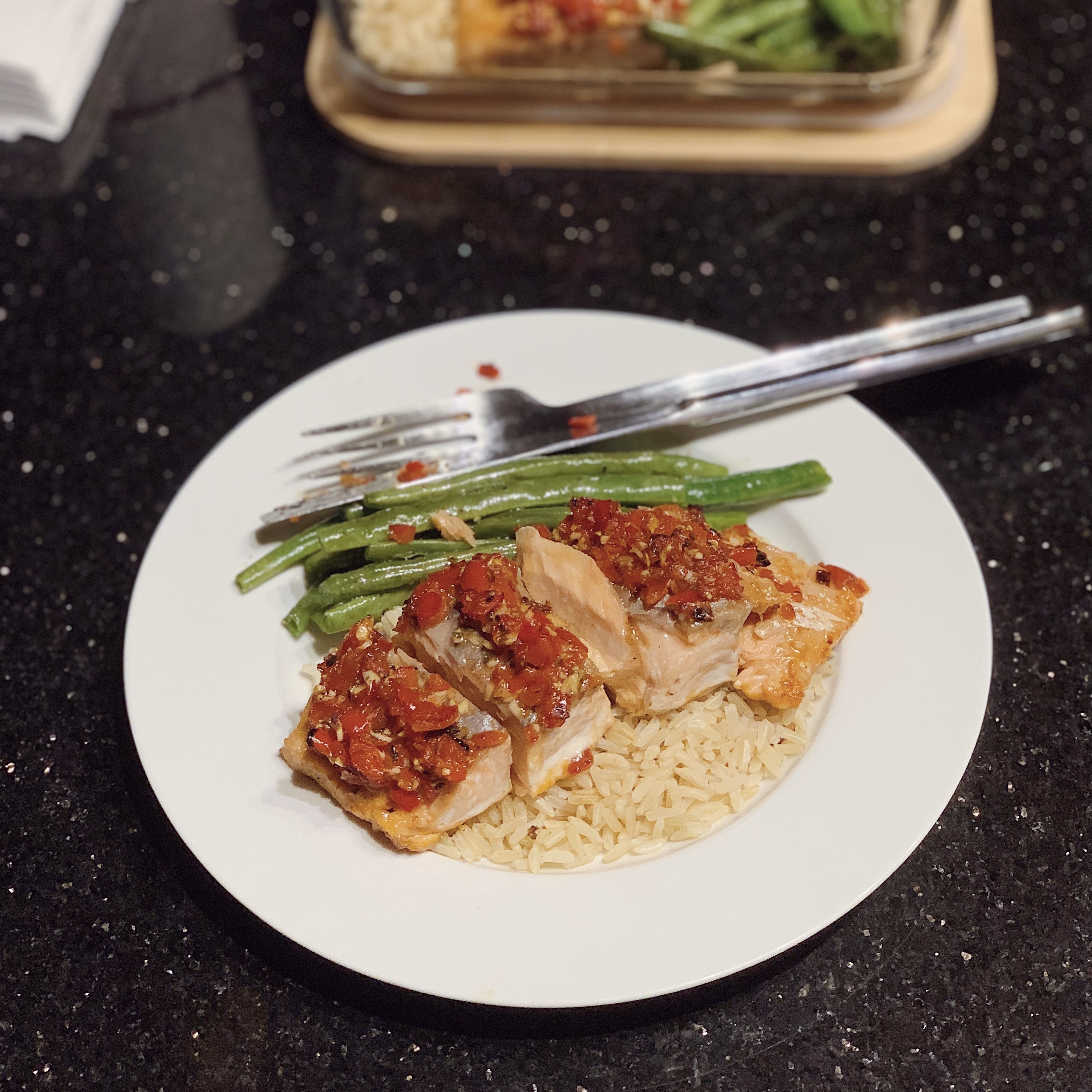 A plate of Roasted Red Pepper Salmon, with a bed of brown jasmine rice, chopped salmon and roasted green beans.