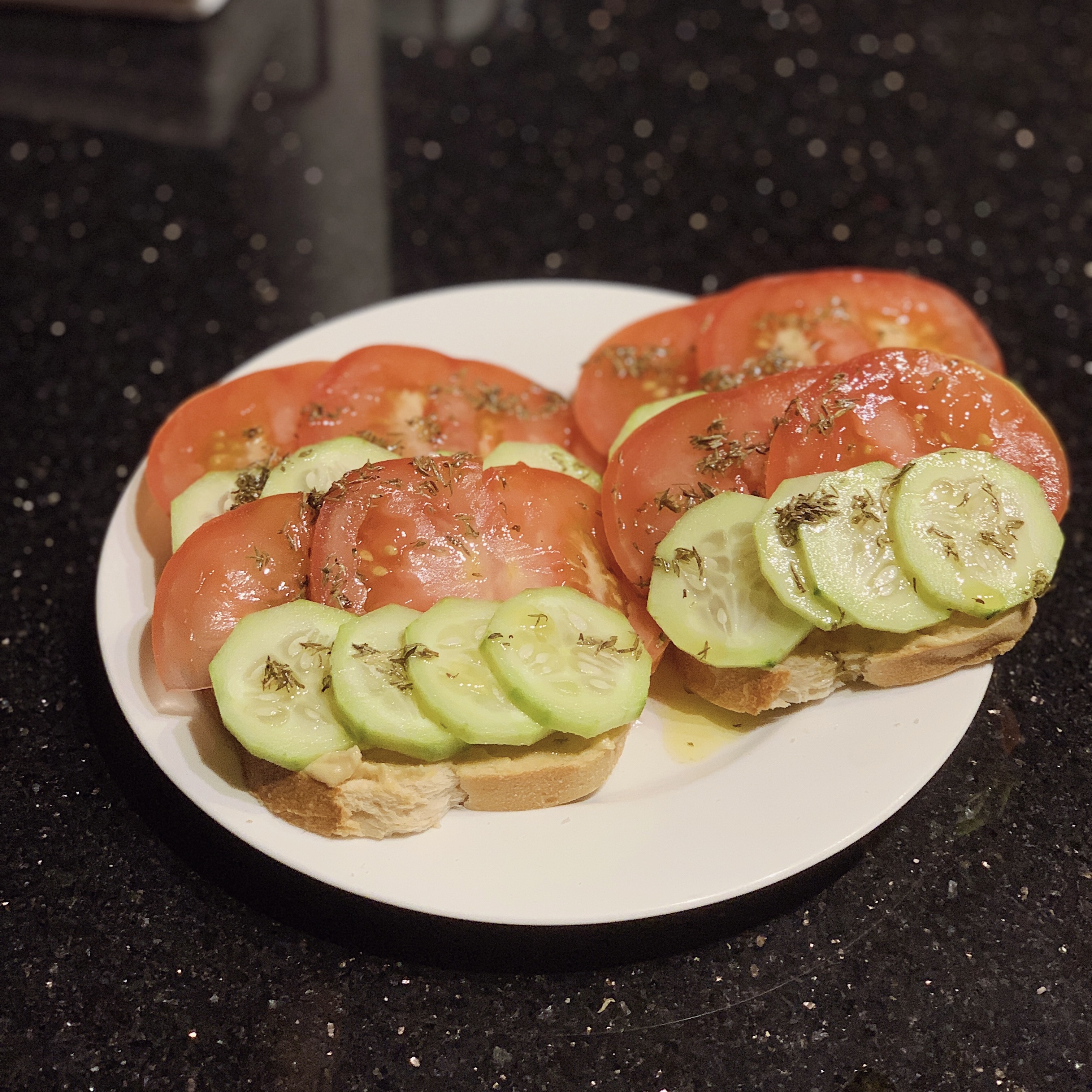 A plate of Hummus Toast; two slices of bread topped with hummus and slices of tomato and cucumber.