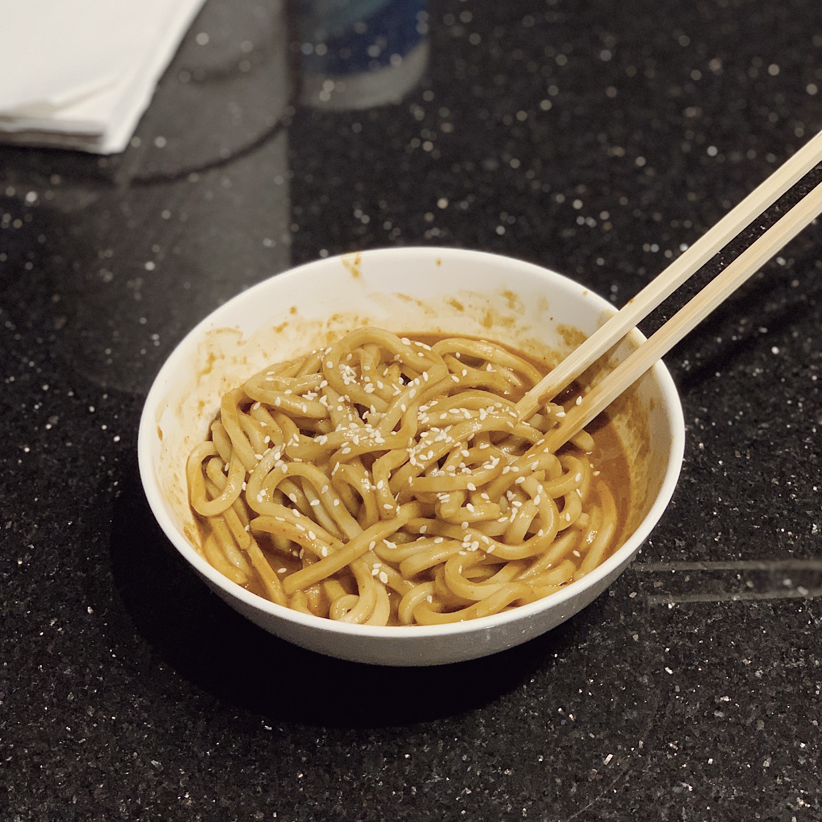 A bowl of Spicy Garlic Peanut Butter Udon noodles with chopsticks.